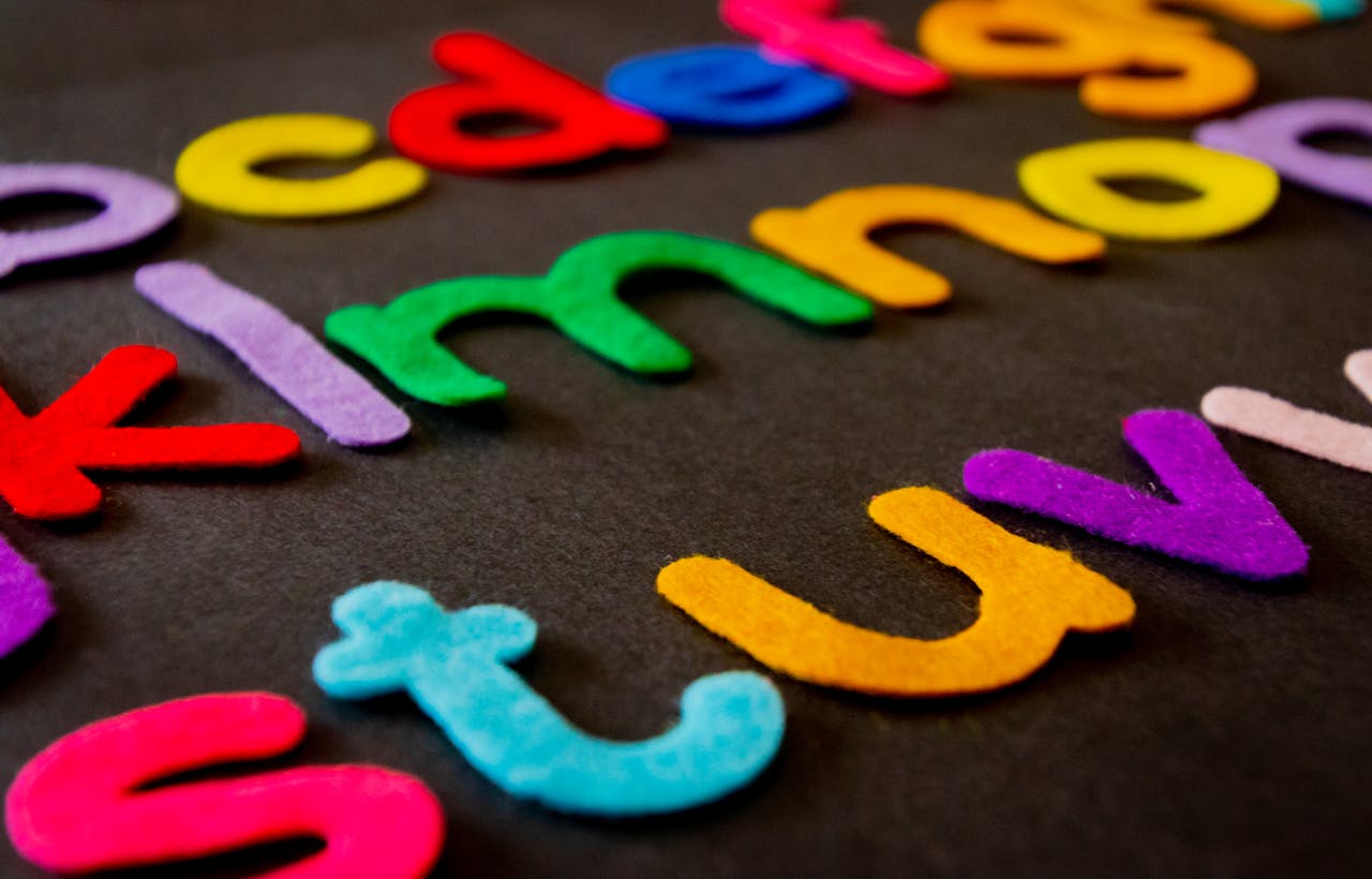 about-02 Bright and colorful felt alphabet letters arranged on a dark surface, perfect for educational and creative projects.