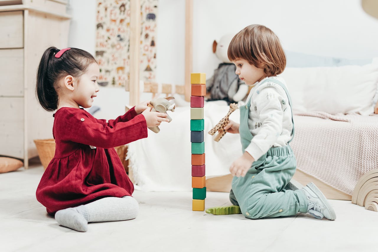 service-03 Two young children enjoying playtime with wooden blocks in a cozy indoor setting, fostering creativity and fun.