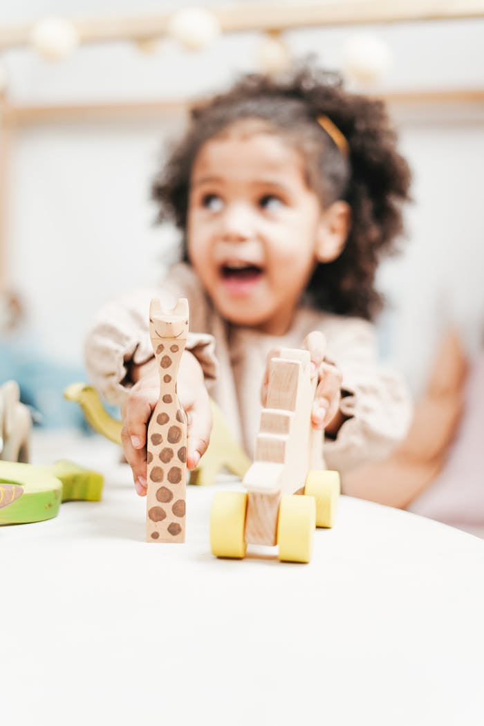 A happy child with curly hair enjoys playing with wooden toys in a bright indoor setting.